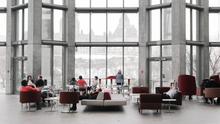 Several people sit in chairs in front of a window overlooking the Parliament of Canada