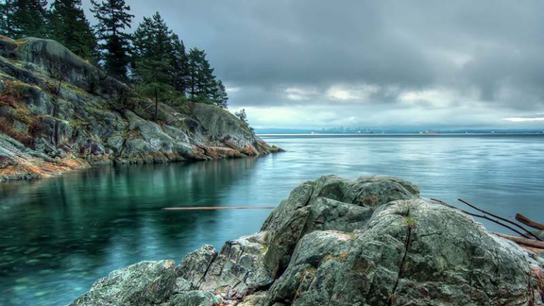 Un ciel nuageux au-dessus de l'océan, de la côte rocheuse et des conifères de Bowen Island, en Colombie-Britannique.